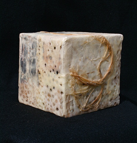Box covered with various papers, wax, paint rags, and twine with burned-in holes. 