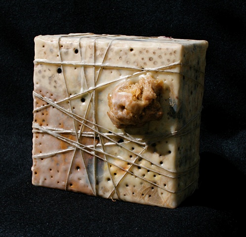 Box covered with various papers, wax, paint rags, with burned-in holes. 