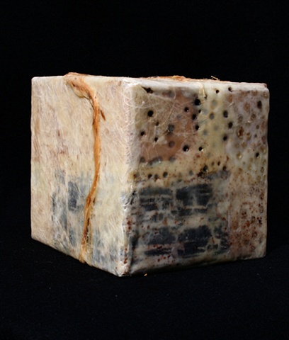 Box covered with various papers, wax, paint rags, and twine with burned-in holes. 