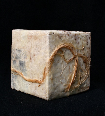 Box covered with various papers, wax, paint rags, and twine with burned-in holes. 