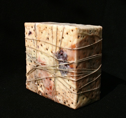 Box covered with various papers, wax, paint rags, with burned-in holes. 