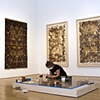Installation in progress, with prints on the back wall and original rugs to the left.
